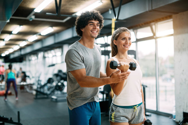 Young beautiful woman doing exercises with personal trainer in gym - Photo, Image