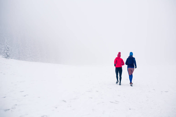 Duas mulheres trilha correndo na neve em montanhas de inverno
 - Foto, Imagem