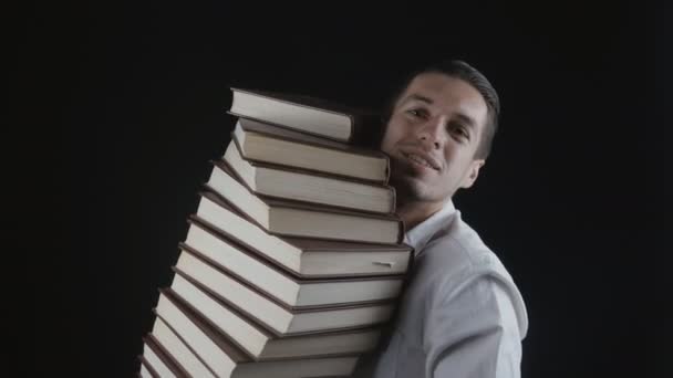 Man in een wit overhemd houdt een stapel boeken in zijn handen in een donkere kamer. Jonge zakenman met boeken in handen. - Video