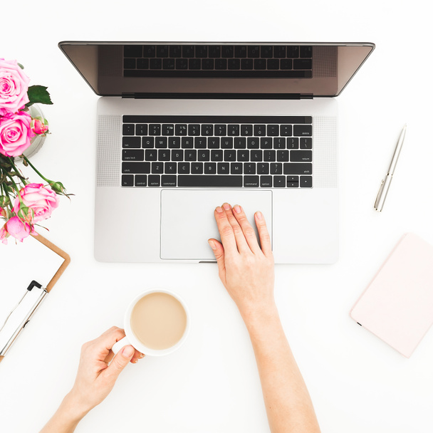 Woman workspace with female hands, laptop, pink roses bouquet, coffee mug on white table - Photo, Image