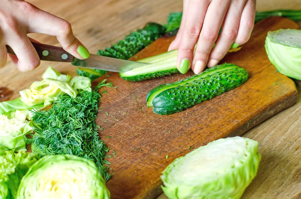 Female hands cutting fresh green cucumbers on a wooden cutting board - Photo, Image