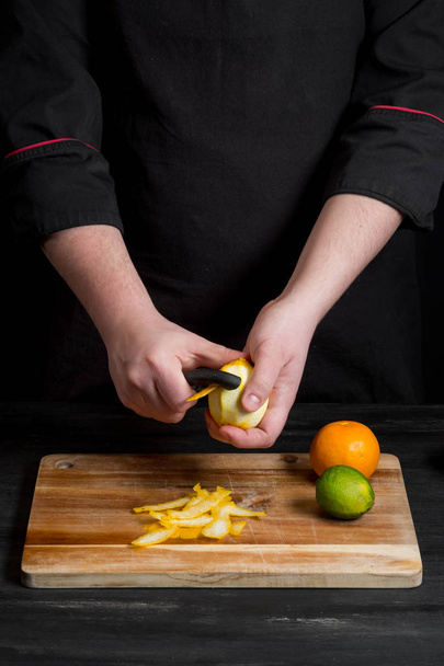 chef hands peeling lemon with knife over wooden board. - Fotografie, Obrázek