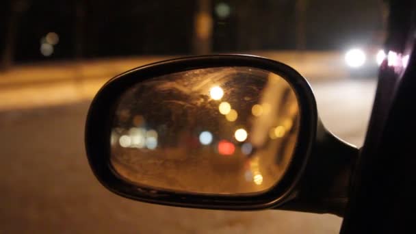 Autók és gyalogosok tükröződik a tükörben az autó oldalnézetből este a város utcáján. - Felvétel, videó