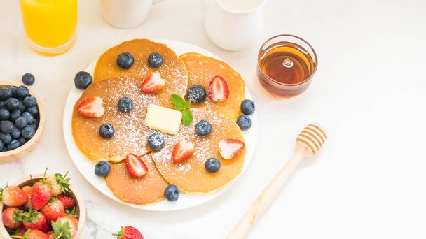 Set de petit déjeuner sain avec Crêpes aux myrtilles et fraises et café noir, Lait et jus d'orange sur fond de table en pierre blanche
 - Photo, image