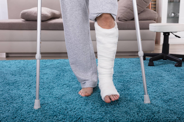 Man With Broken Leg Using Crutches For Walking On Blue Carpet - Valokuva, kuva