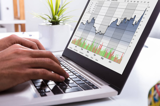 Nahaufnahme der Hand eines Börsenmaklers bei der Analyse von Graphen auf dem Laptop im Büro - Foto, Bild