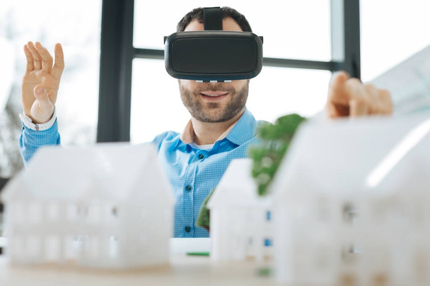 Веселый мужчина в гарнитуре VR смотрит на моделей домов
 - Фото, изображение