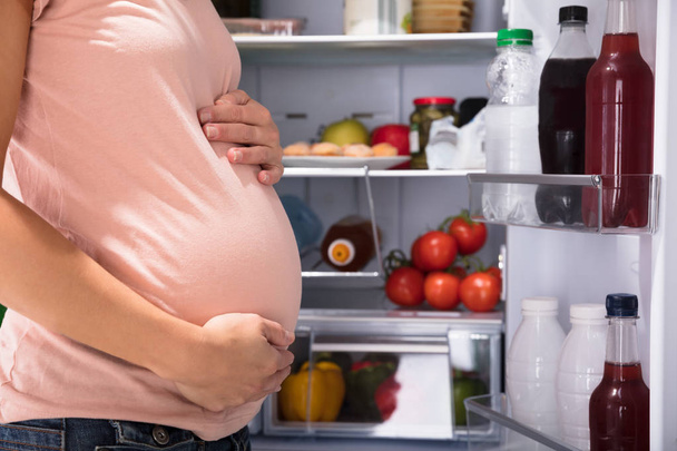 Close-up Of Pregnant Woman Standing Near Refrigerator Full Of Healthy Food - Фото, зображення