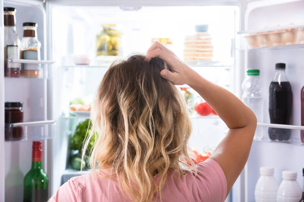 Egy zavaros nő keresi a nyitott hűtőszekrény otthon hátulnézet - Fotó, kép