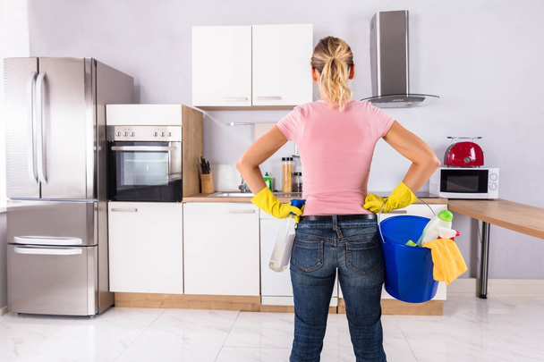Woman Wearing Gloves Carrying Cleaning Equipments In Bucket Standing In Kitchen - Фото, зображення