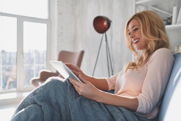 smiling blonde woman using digital tablet and sitting on sofa at home - Photo, Image