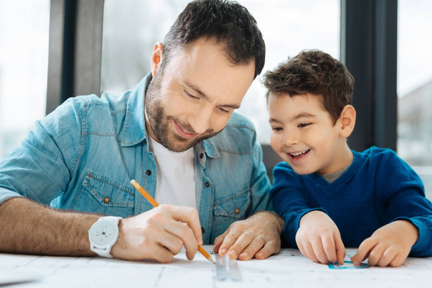 Joyful boy watching his father drawing blueprint - Foto, afbeelding