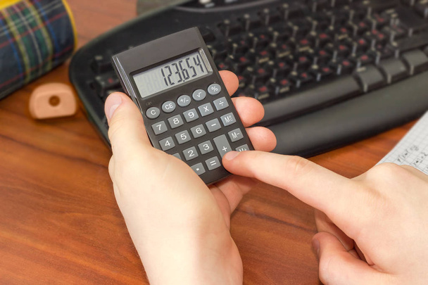 Ηλεκτρονική αριθμομηχανή στο χέρι του μαθητή πάνω από την επιφάνεια εργασίας - Φωτογραφία, εικόνα