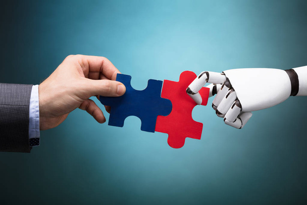 Podnikatel a robota drží Jigsaw Puzzle na tyrkysové pozadí - Fotografie, Obrázek
