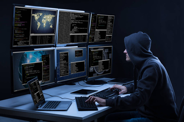 Rear View Of A Hacker Using Multiple Computers For Stealing Data In Office - Photo, Image