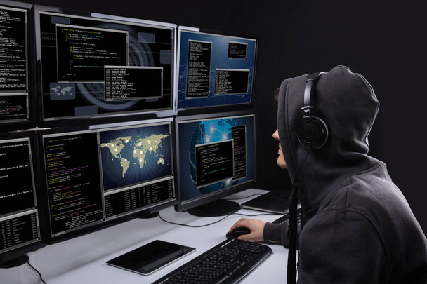 Rear View Of A Hacker Using Multiple Computers For Stealing Data In Office - Foto, Bild