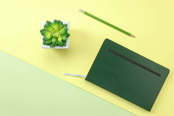 Тетрадь и ручка с кактусом в белом горшке на современном желтом и зеленом фоне с пространством
. - Фото, изображение