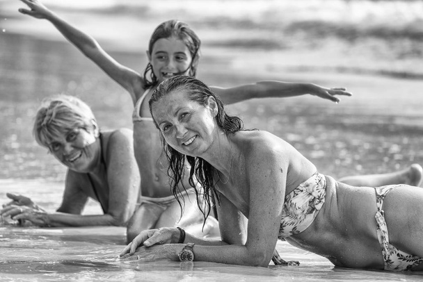 Tres generaciones femeninas felices y sonrientes, tendidas en la costa
. - Foto, Imagen