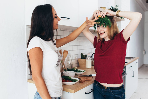 Las mujeres en la cocina bromean, se ríen y se divierten. Jugando con verduras
 - Foto, imagen