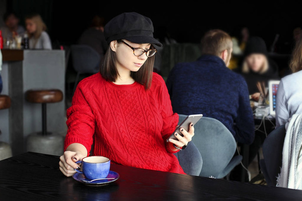 Szczęśliwa młoda kobieta picia latte, macchiato, cappuccino, herbata, przy użyciu komputera typu tablet i rozmawia przez telefon, kawiarnia / bar. - Zdjęcie, obraz
