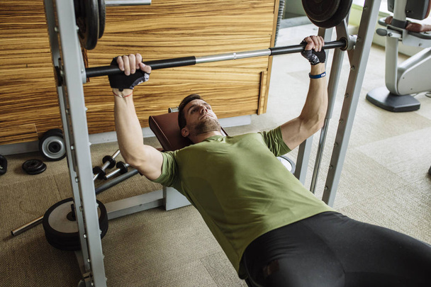 Handsome Caucasian man lifting weights at gym. - Фото, изображение