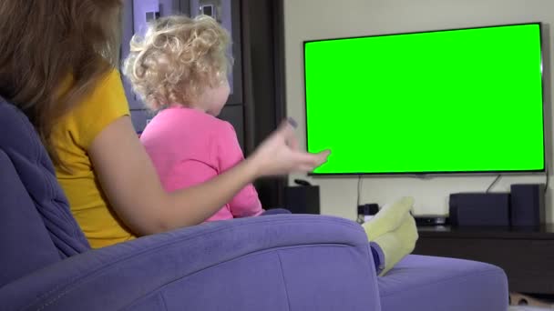 klein kind kijken Tv-programma met moeder. Groene chroma key scherm - Video