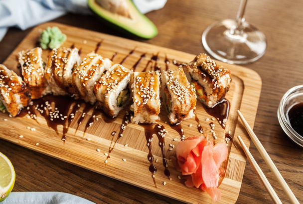Rotoli di sushi giapponese con wasabi, salsa di soia allo zenzero e bacchette e un bicchiere di vino su una tavola di legno
 - Foto, immagini