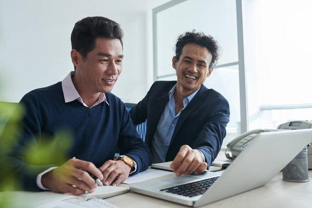 Nauravat aasialaiset liikemiehet katselevat jotain hauskaa kannettavan tietokoneen näytöllä
 - Valokuva, kuva