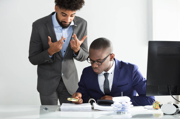 Man With Fingers Crossed Looking At Young African Auditor Analyzing Bill At Workplace - Foto, Bild