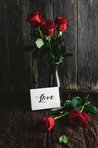 Red roses in vase and Love greeting card on shabby wooden background, valentines day concept - Photo, Image