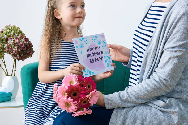 Happy Mother's Day. Cute little girl giving mom greeting card, present and bouquet of pink gerbera daisies. Mother and daughter concept. - Valokuva, kuva