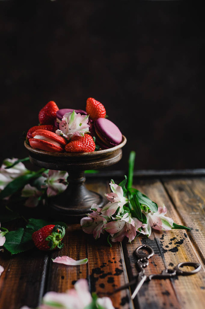 bowl with macarons and strawberries on wooden table with flowers and scissors - Foto, Bild
