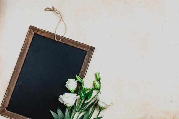 top view of blackboard in wooden frame with eustoma flowers on shabby background - Foto, Imagen