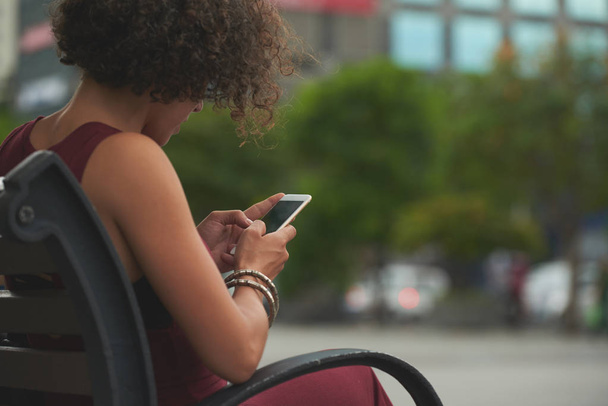Kobieta siedzi na ławce i SMS-y, widok na ramieniu - Zdjęcie, obraz
