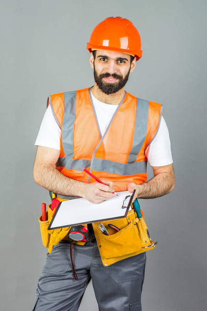 A builder in an orange helmet on a gray background signs somethi - Foto, afbeelding