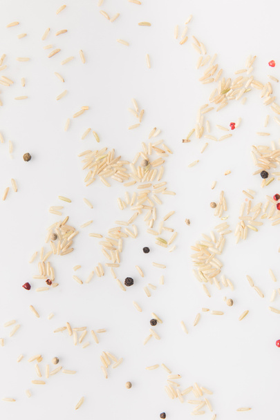 top view of spilled raw rice with peppercorns on white surface - Photo, Image