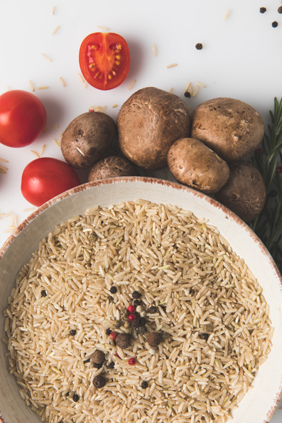 vue du dessus du riz cru et des épices dans un bol avec des champignons et des tomates sur la surface blanche
 - Photo, image