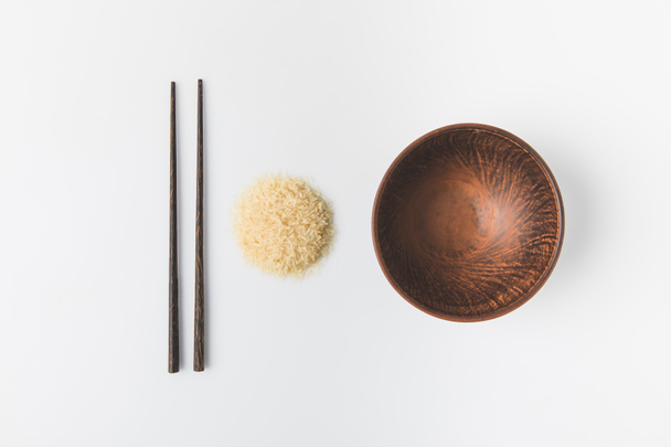 bovenaanzicht van rauwe rijst berg met kom en eetstokjes geïsoleerd op wit - Foto, afbeelding