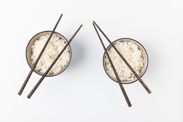 top view of bowls of tasty rice with chopsticks isolated on white - Fotó, kép