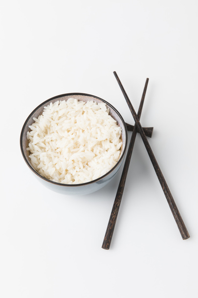 Schüssel mit frisch gekochtem Reis mit Essstäbchen auf weißer Tischplatte - Foto, Bild
