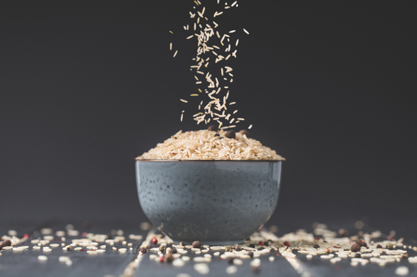 side view of rice spilling into bowl on black table - Photo, Image