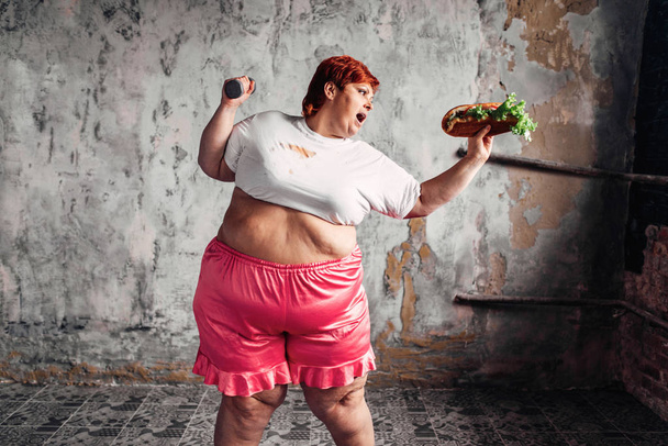 overweight woman with dumbbell and sandwich in hands, fight against obesity concept, overweight problem - Photo, image
