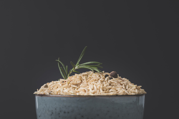 close-up shot of bowl of raw rice with rosemary and spices on black surface - Fotoğraf, Görsel