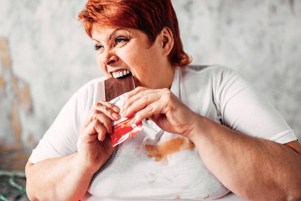 Ylipainoinen nainen syö suklaata, laiskuutta ja lihavuutta. Epäterveellistä ruokaa syöminen
 - Valokuva, kuva