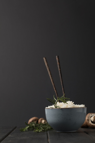 bowl of tasty rice with chopsticks and mushrooms on black tabletop - Fotó, kép