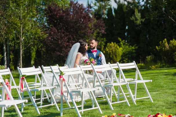 Hermosa pareja casada sentada una de las sillas de madera blanca de la boda para invitados
 - Foto, imagen