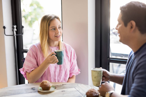 Beautiful young blonde drinking coffee and talking with her boyfriend at a restaurant - Photo, Image