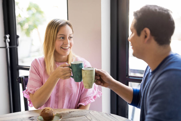 glückliches junges Paar, das eine gute Zeit zusammen hat und mit einer Tasse Kaffee in einem Café anstößt - Foto, Bild