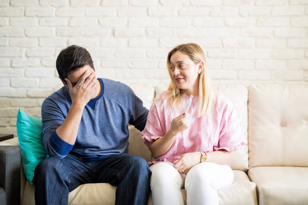 Young man feeling worried after knowing pregnancy test results from his girlfriend sitting on a couch at home - Photo, Image