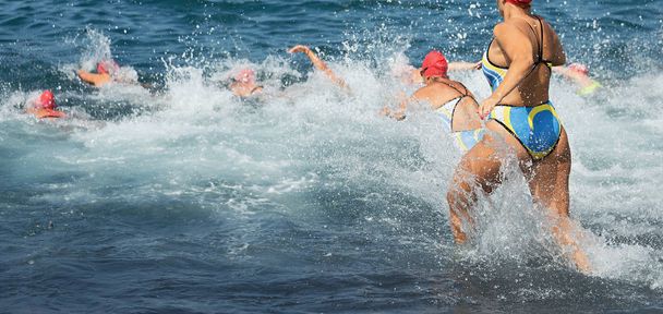 Участники группового триатлона бегут в воду на заплыв, брызги воды и бегущие спортсмены
 - Фото, изображение